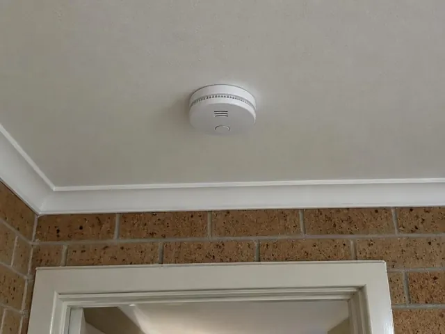 Ceiling-mounted smoke alarm above a doorway in a brick-walled home interior in Shelly Beach